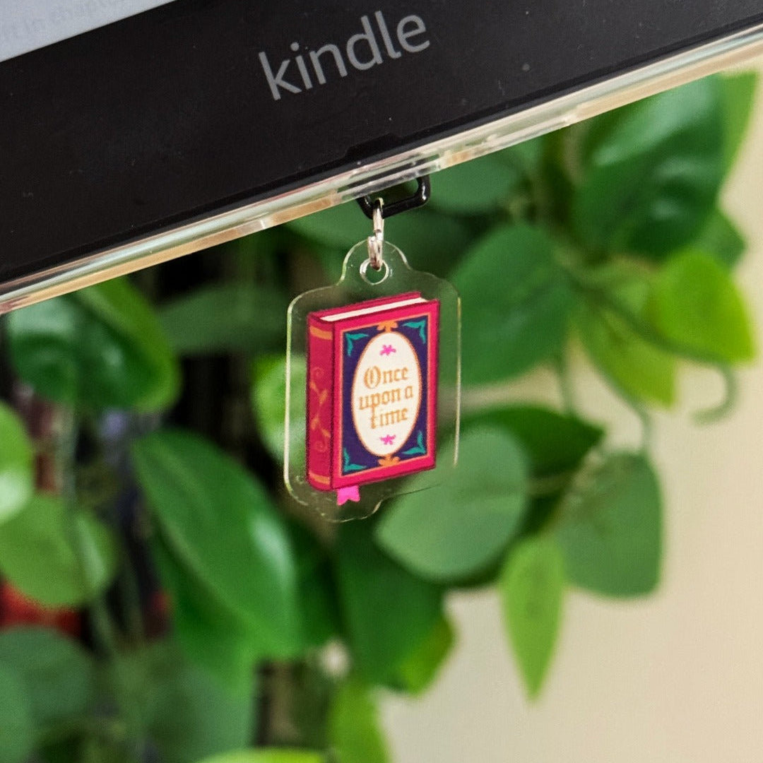 Decorative charm shaped like a book with 'Once upon a time' text hanging from a Kindle device.