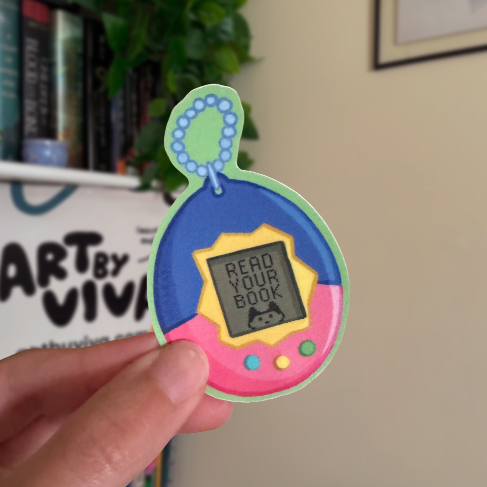 Colorful toy with 'Read Your Book' message held by a hand, with books and a plant in the background.